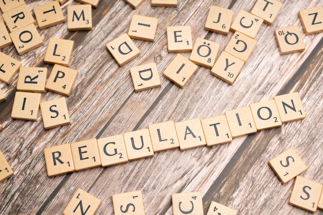 hero-img-01 Wooden letter tiles spelling 'Regulation' on a textured wood background, conveying themes of compliance and structure.